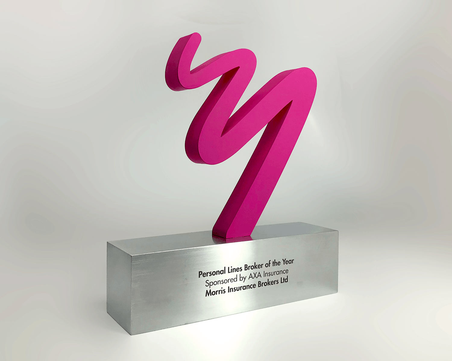 A modern abstract award trophy featuring a vibrant magenta pink wavy sculpture mounted on a brushed silver rectangular base with engraved text, set against a clean light gray studio background.
