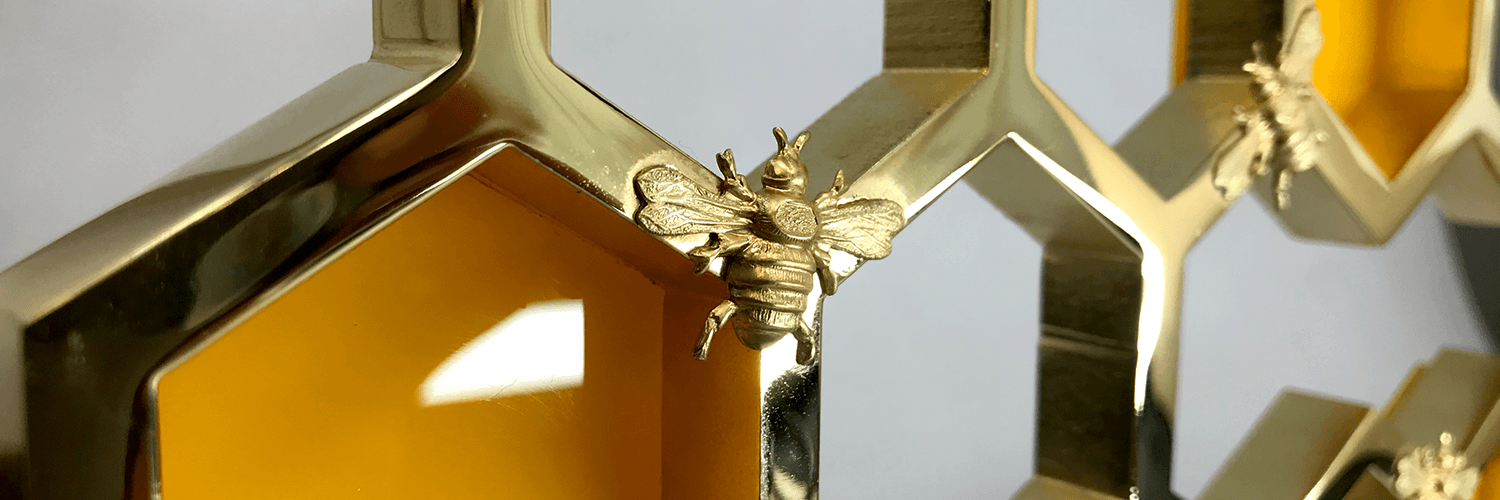 Close-up of a polished gold honeycomb trophy with small bee figures on the hexagonal frame, lit with a warm amber glow.