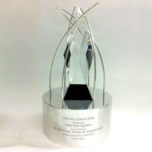 Silver and cut glass trophy with engraved text on a white background