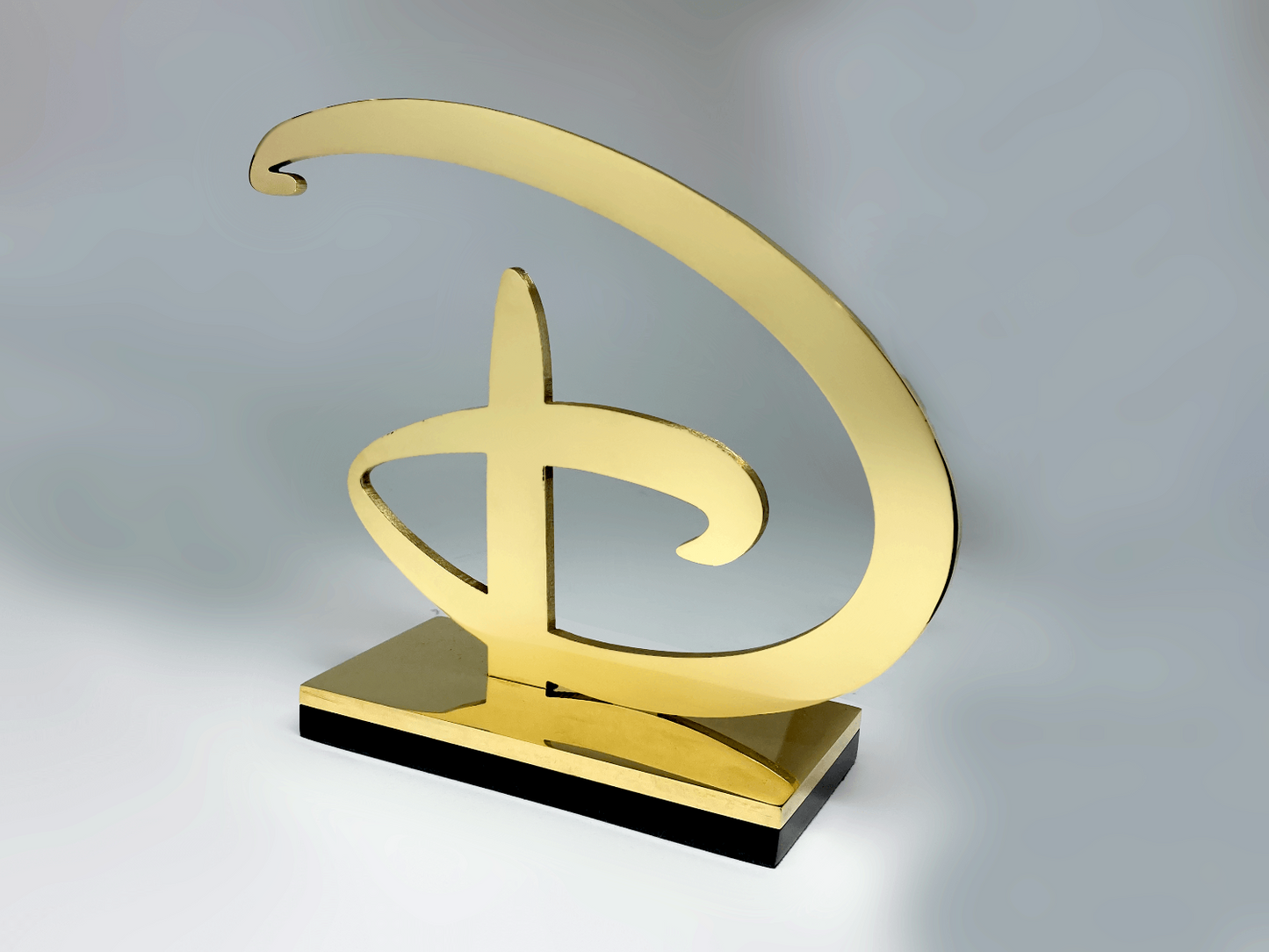 Polished brass Disney logo sculpture, side angle showing freestanding curved signature form
