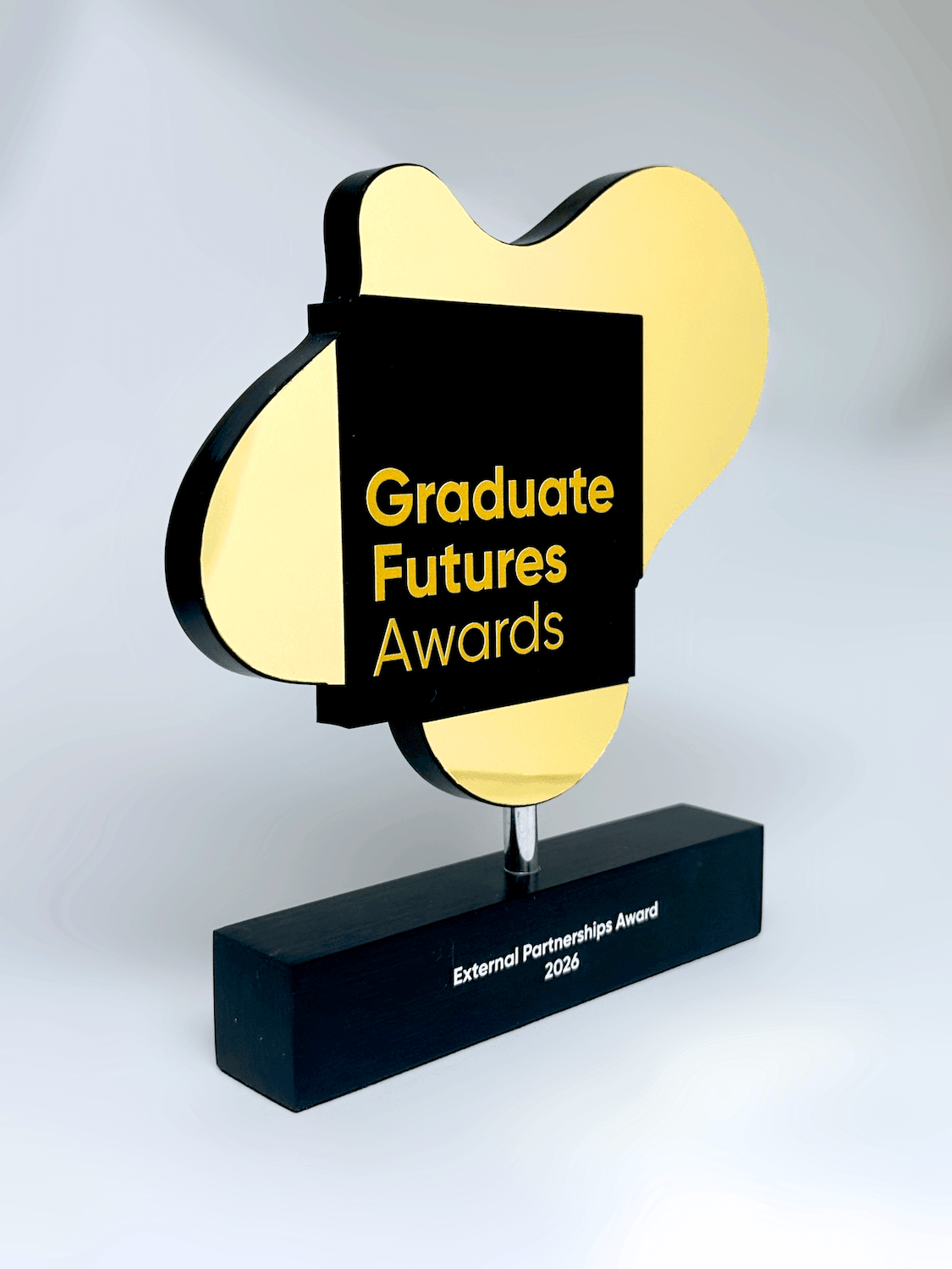 An award trophy with a black rectangular base engraved with 'External Partnership Award 2026', featuring a gold abstract shape behind a central black panel with yellow text reading 'Graduate Futures Awards'.