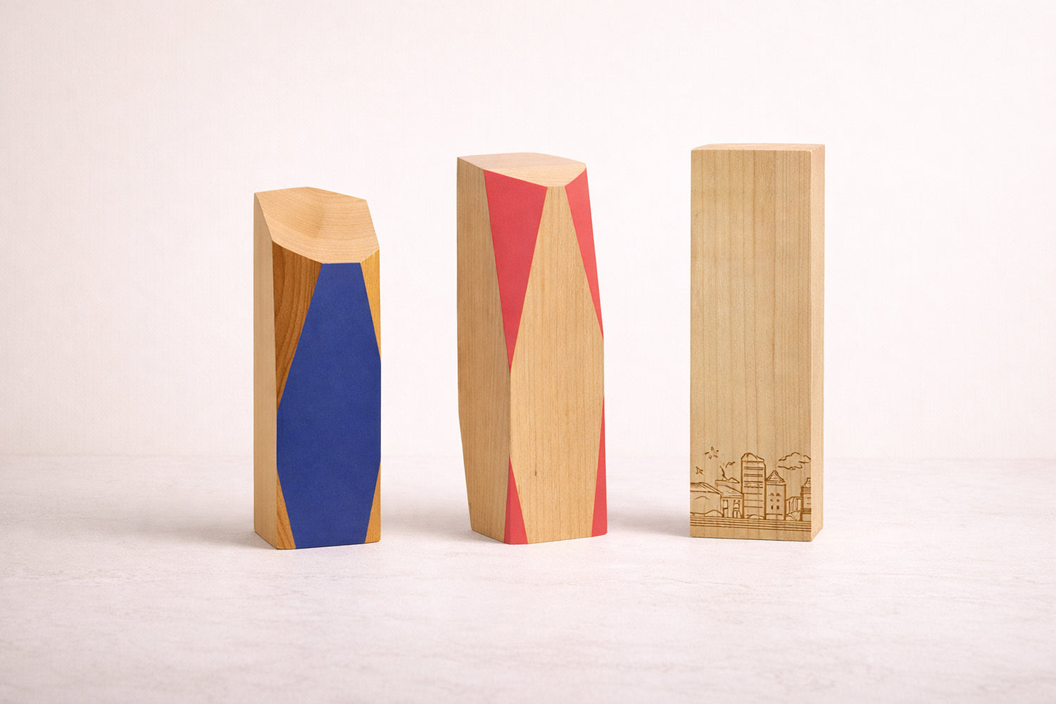 Three wooden off the shelf awards with colourful geometric designs on a white background