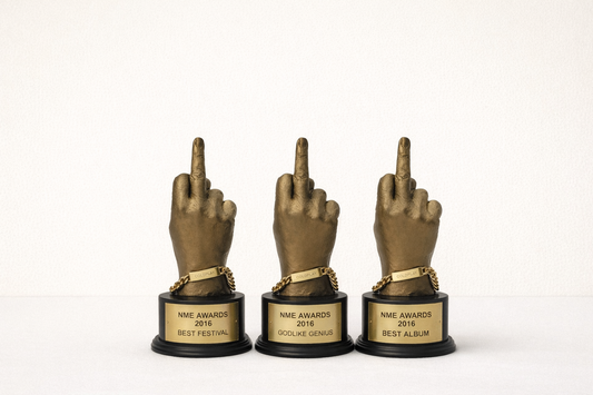 Three NME 2016 BRAT awards with middle finger gestures on a white background