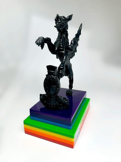 City of London Police and National LGBT+ Police Network for Pride Week griffin figurine standing on a tiered rainbow-colored acrylic base against a white studio background.