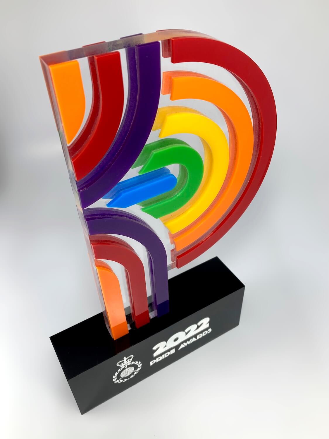 Three-quarter view of bespoke rainbow pride award, precision-cut acrylic layers on custom black engraved plinth