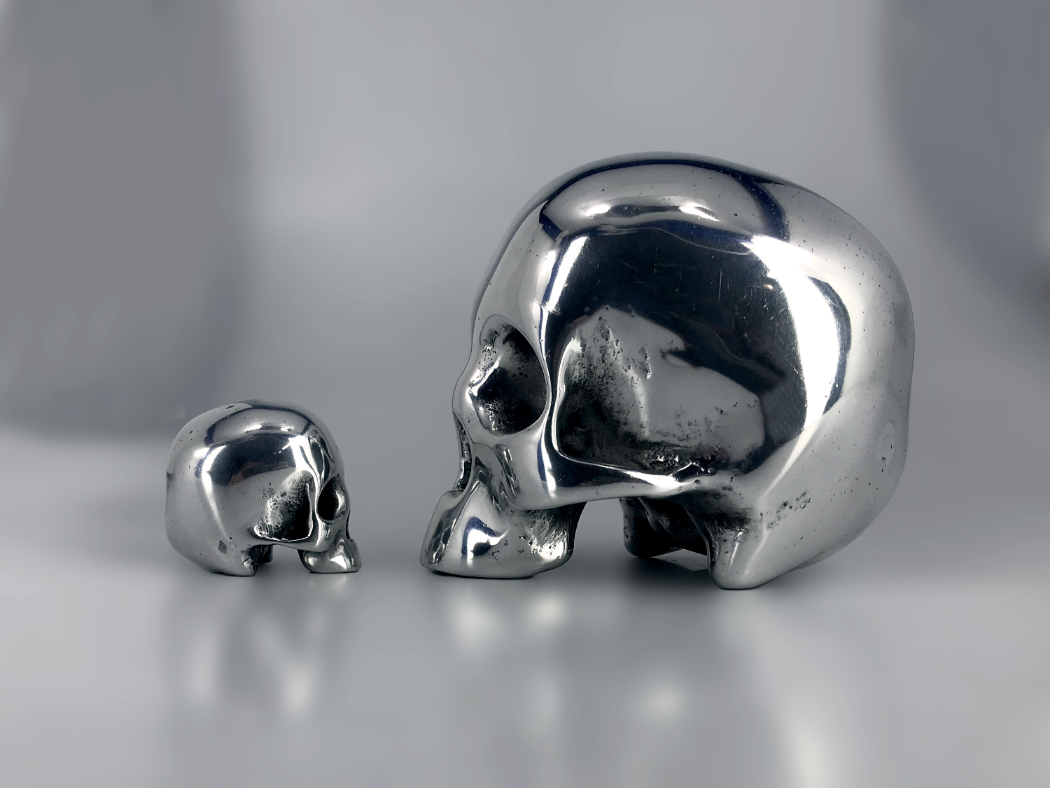 Two metallic skull awards on a reflective surface with a blurred background