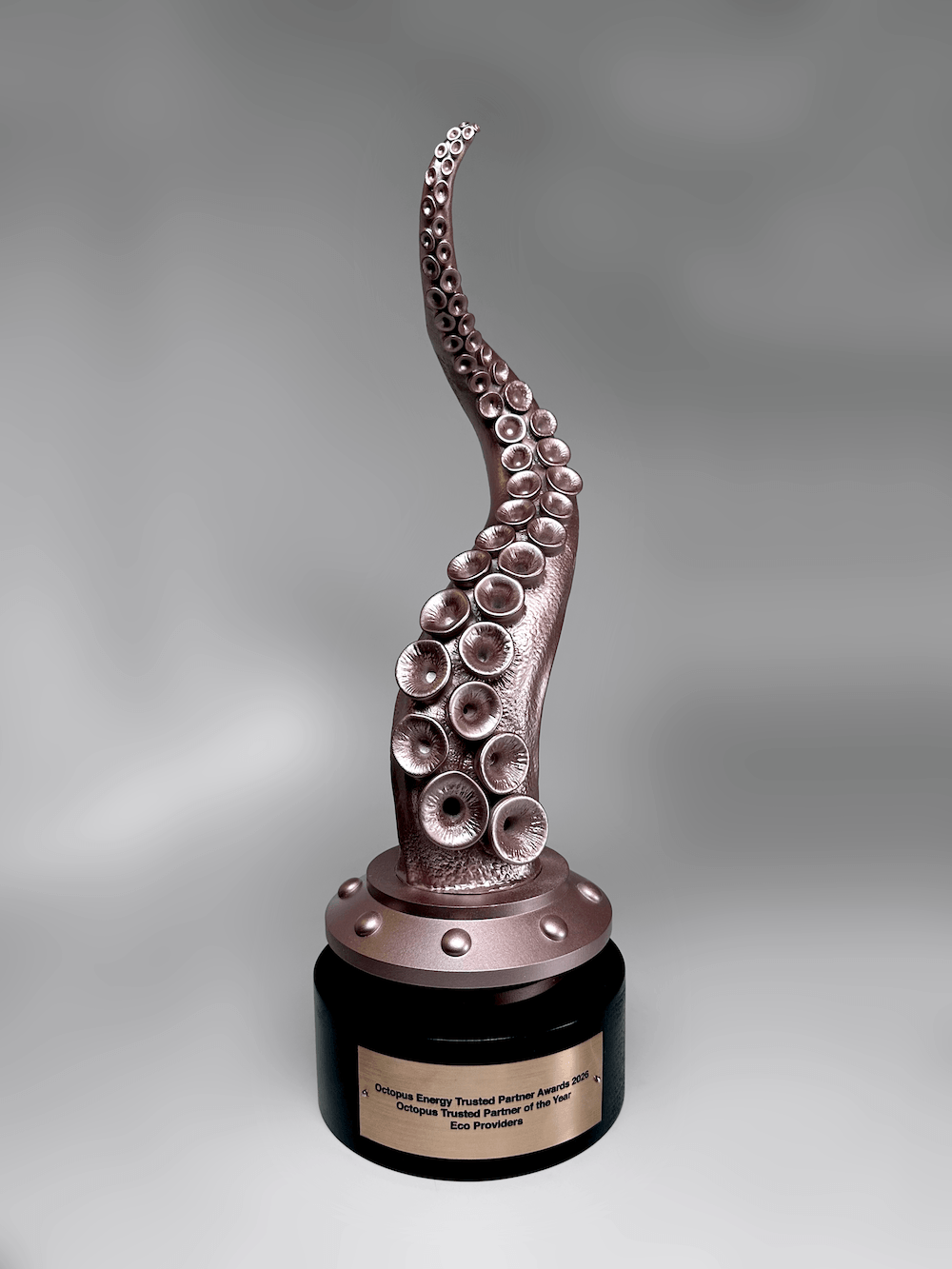 An octopus tentacle award sculpture with realistic suction cups, mounted on a metallic bronze base and a round black pedestal with a gold nameplate, photographed against a neutral gray gradient background.