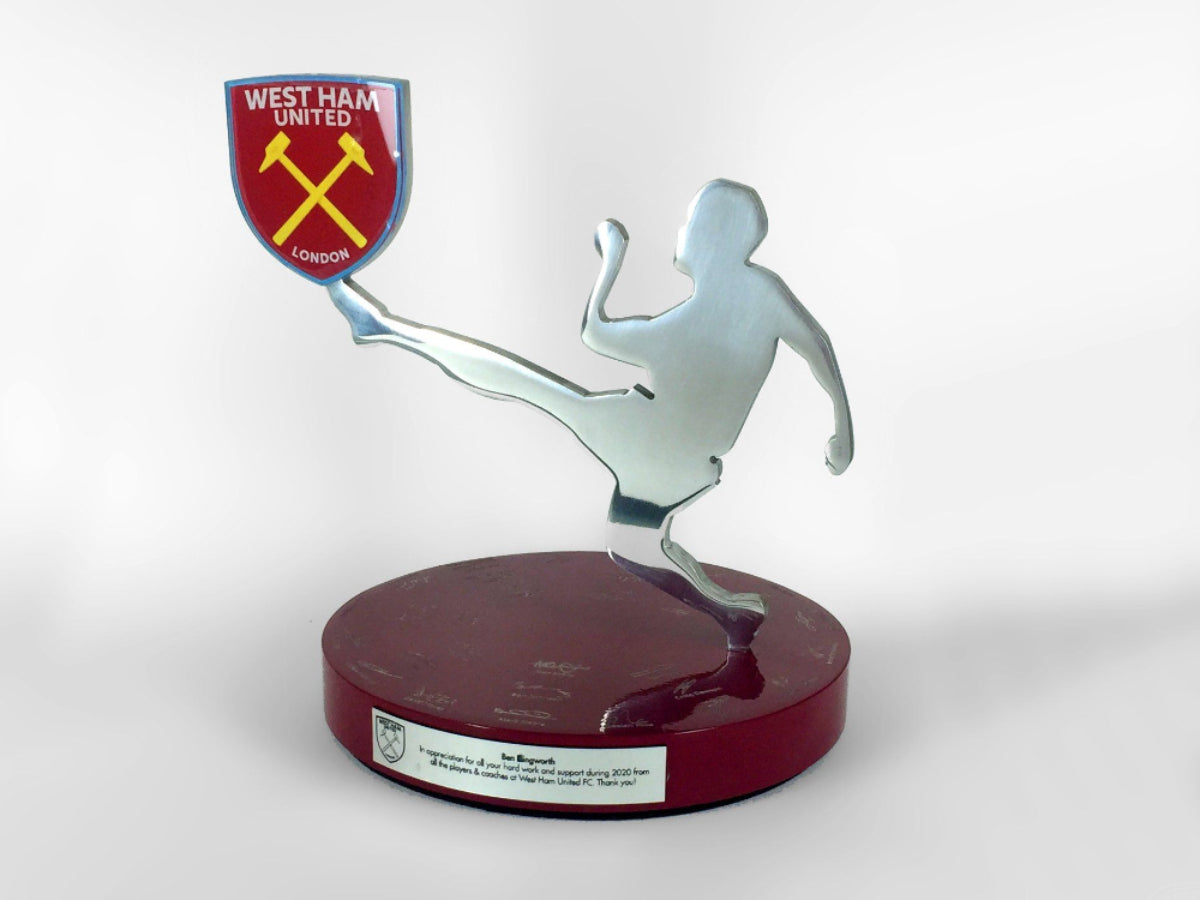 A wooden based award with a metal footballer kicking a west ham logo.