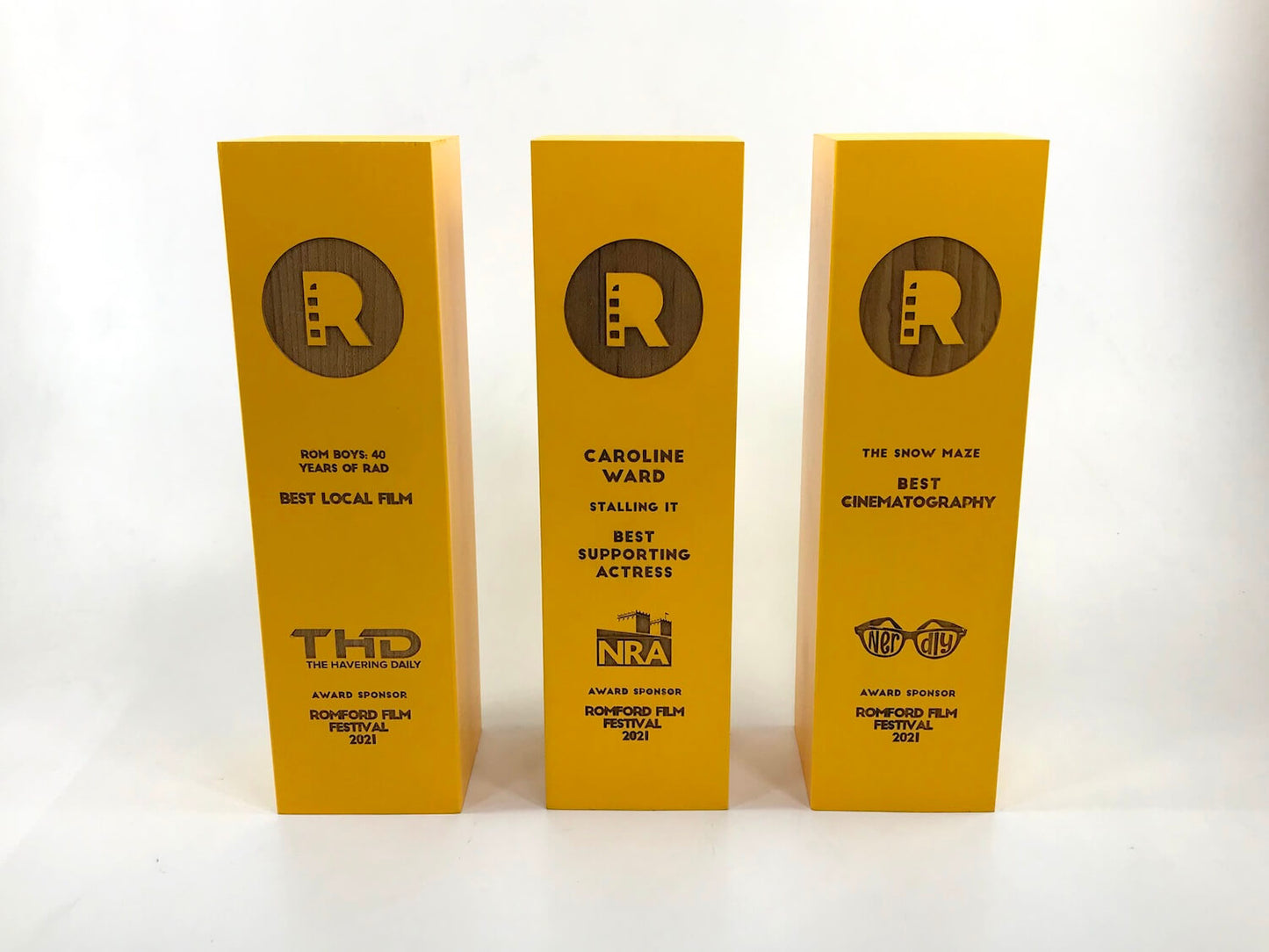 Three gold Romford Film Festival award plaques standing upright on a white surface against a white background.