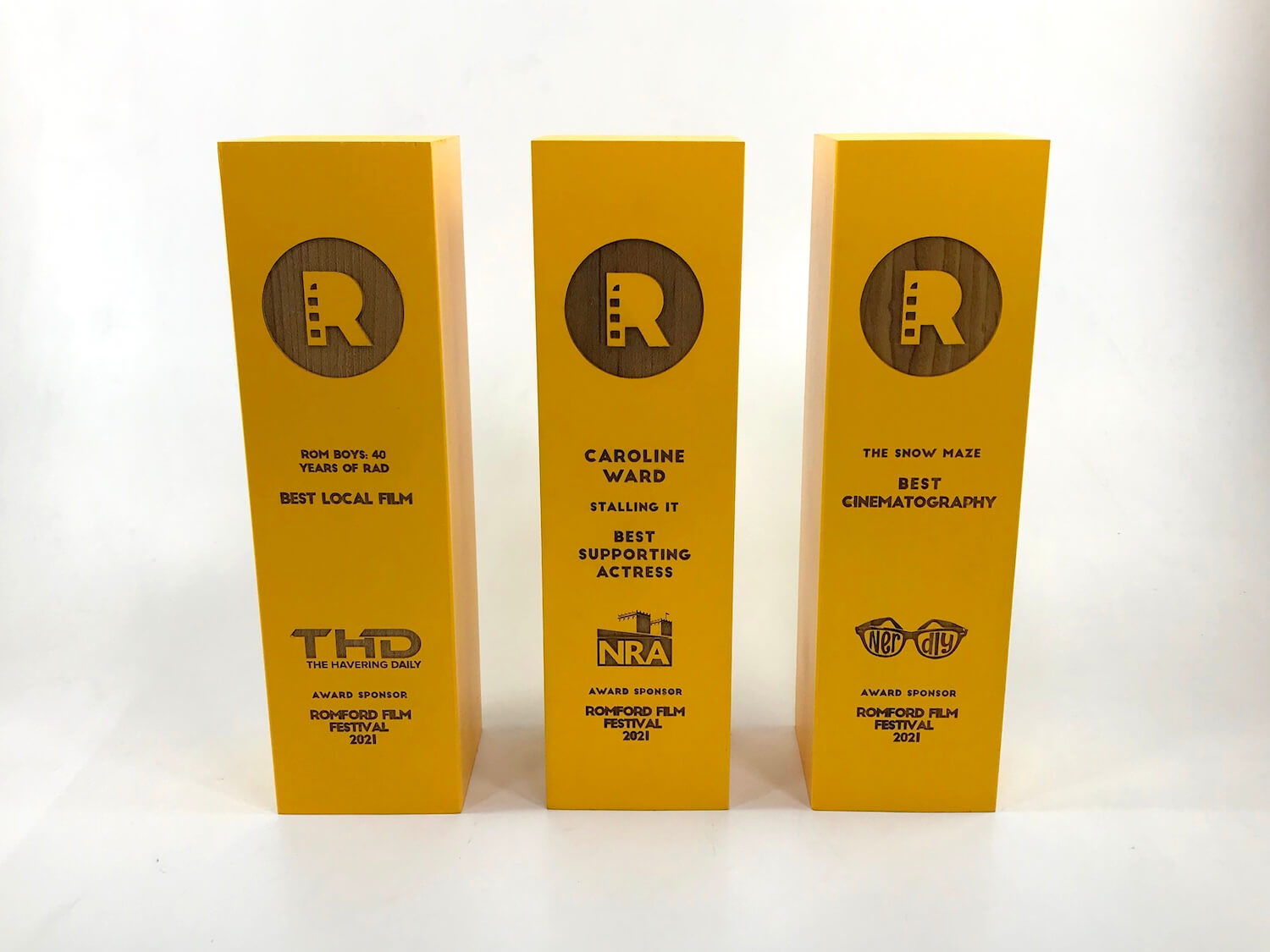 Three gold Romford Film Festival award plaques standing upright on a white surface against a white background.