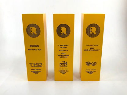 Three gold Romford Film Festival award plaques standing upright on a white surface against a white background.
